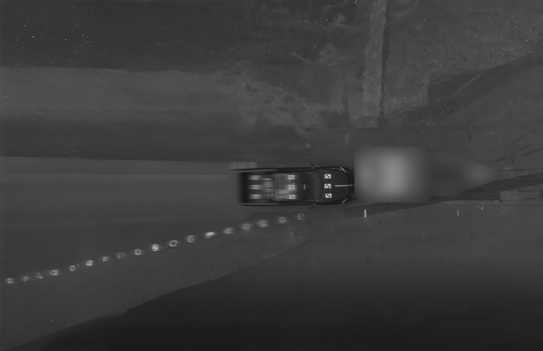Aerial view of a black car driving on a dark road with a blurred section behind it. Circular road markers are visible along the left edge of the road. The image is in black and white.