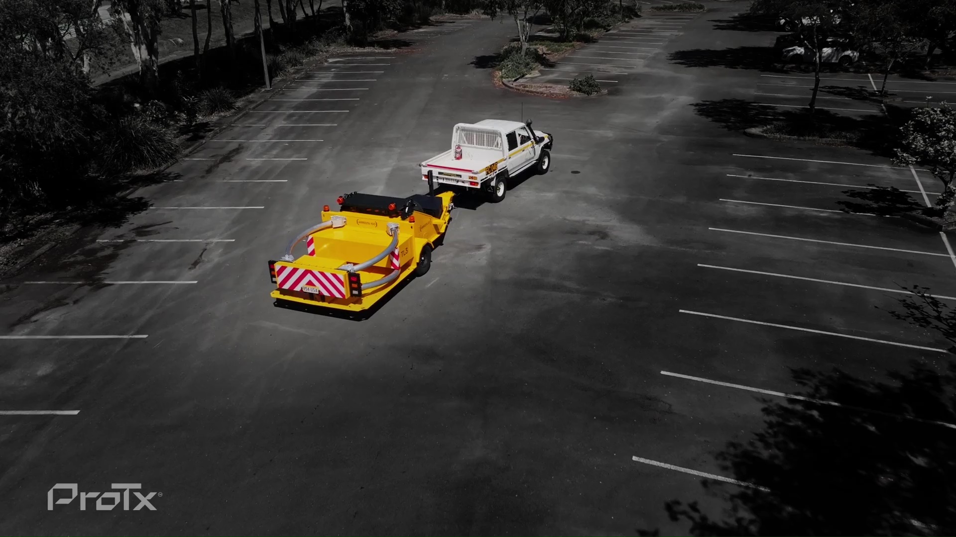 A white truck is towing a bright yellow trailer with red and white reflective stripes in a nearly empty parking lot. The scene is mostly grayscale except for the trailer. The ProTx logo is visible in the bottom left corner.