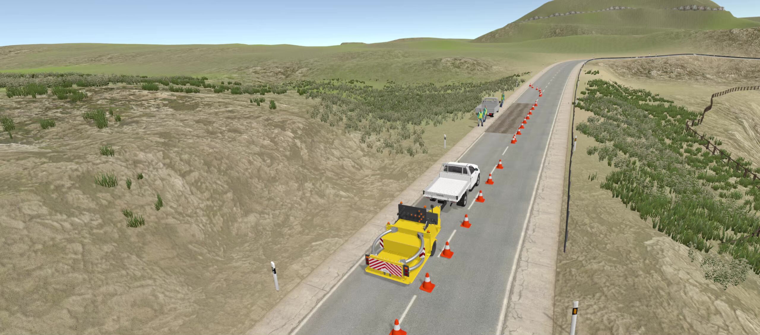 A rural road with traffic cones narrowing one lane. A yellow maintenance truck and a white pickup are parked beside the cones. Grassy hills and sparse vegetation surround the road under a clear sky.