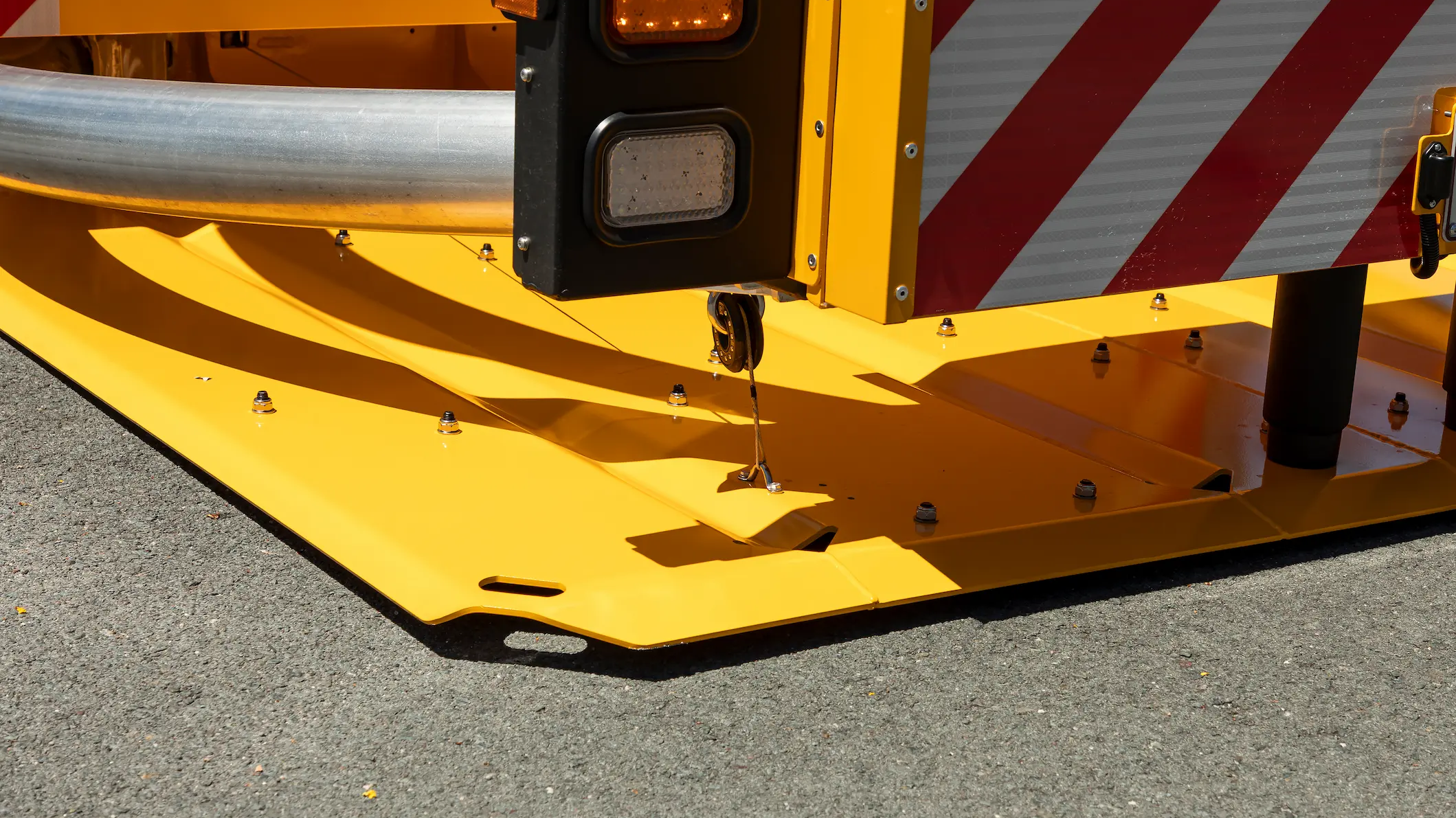 Close-up of a yellow traffic crash cushion base with metal rail, warning lights, and red-and-white striped reflective panel, installed on an asphalt road for vehicle safety.