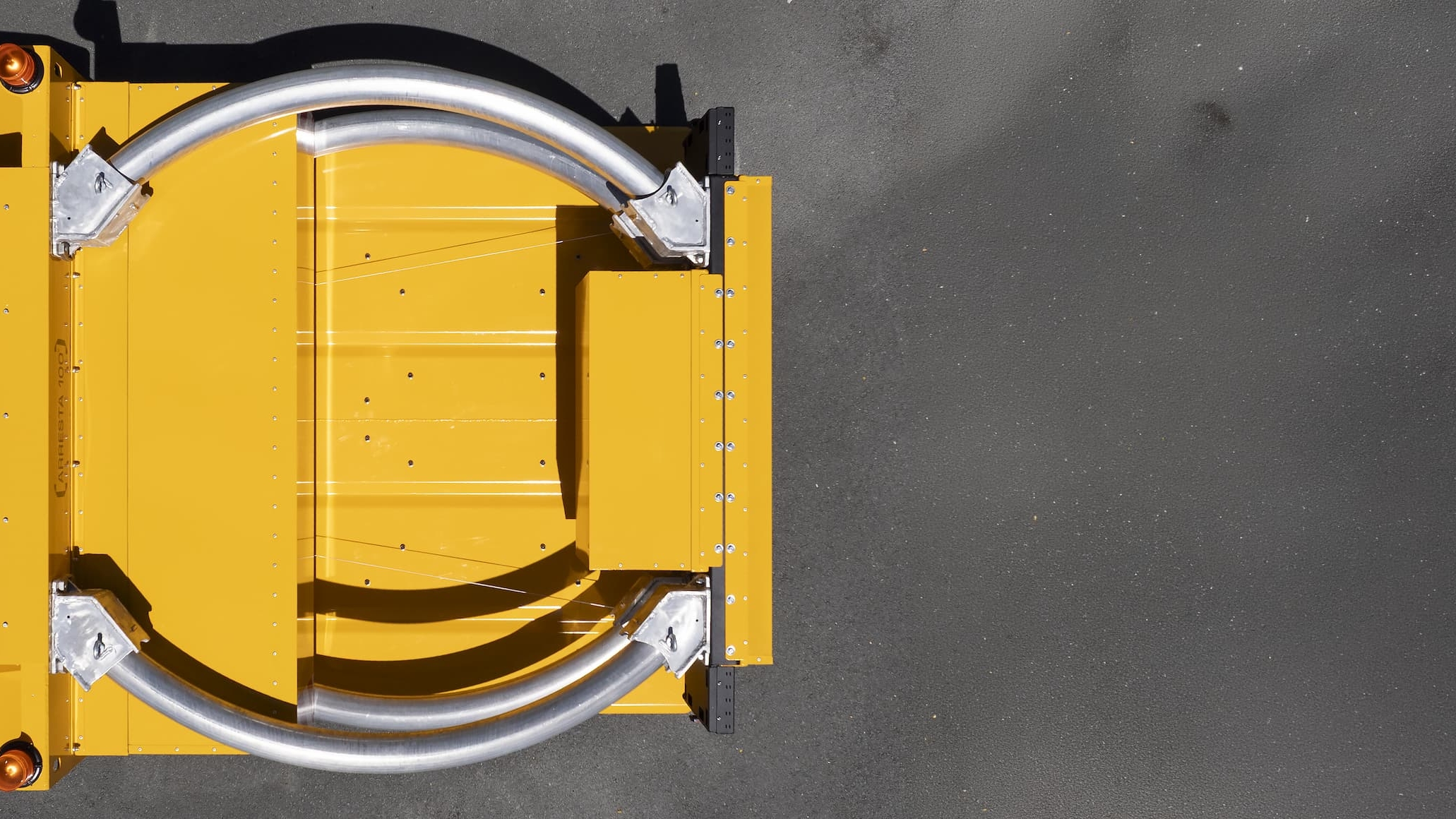 Overhead view of a yellow industrial machine with two large curved silver metal bars on a gray surface, photographed from above with a shadow visible on the right side.